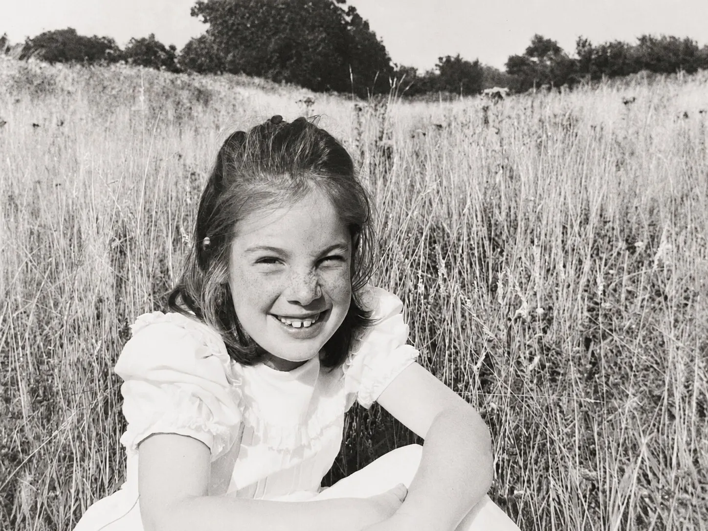 Georgie as a child, sitting in long summer grass