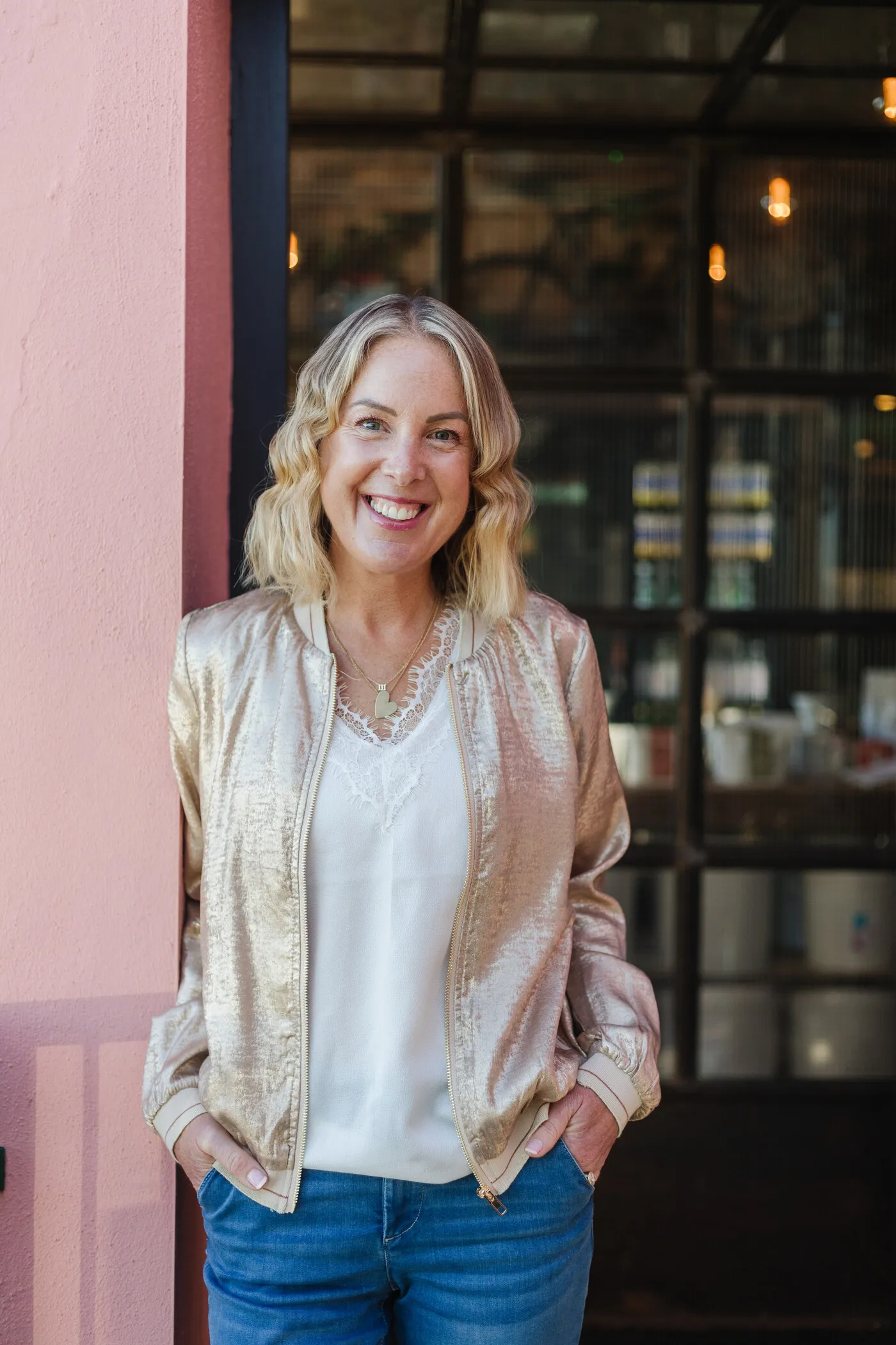 Georgie Durcan laughing, in a gold bomber jacket against a pink wall